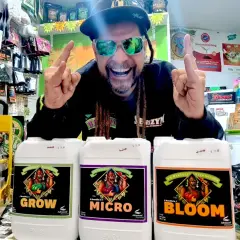 Uomo sorridente con occhiali da sole mostra flaconi di fertilizzanti Advanced Nutrients per la crescita, micro e fioritura.