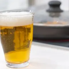 Un bicchiere di birra dorata con schiuma, accanto a una padella coperta. Forse la birra è un fertilizzante per le piante in cucina?