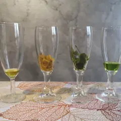 Quattro bicchieri con liquidi colorati e foglie. Il verde brillante suggerisce la clorofilla, essenziale per la fotosintesi.