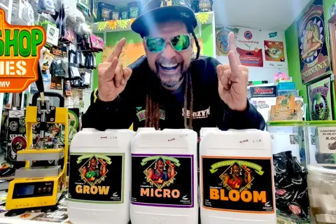 Uomo sorridente con occhiali da sole mostra flaconi di fertilizzanti Advanced Nutrients per la crescita, micro e fioritura.