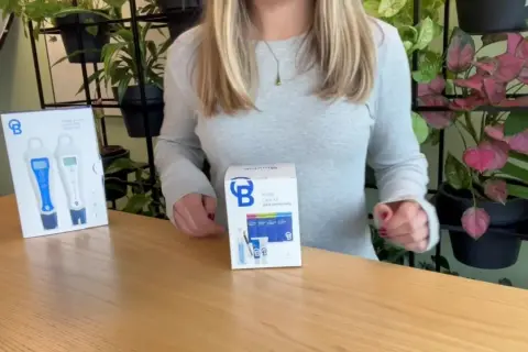Kit di cura per sonde BlueLab con misuratori pH e conducibilità, su un tavolo di legno con piante sullo sfondo.