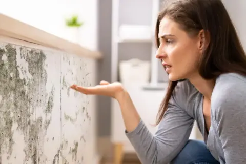 Donna preoccupata osserva muffa su muro, sintomo di umidità 70 per cento in casa.