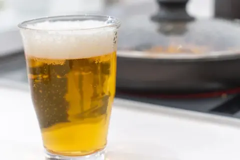 Un bicchiere di birra dorata con schiuma, accanto a una padella coperta. Forse la birra è un fertilizzante per le piante in cucina?
