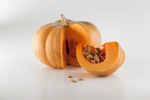 Zucca intera e una fetta con semi, pronti per imparare come piantare i semi di zucca e far crescere un orto autunnale.