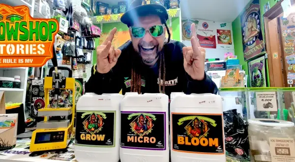 Uomo sorridente con occhiali da sole mostra flaconi di fertilizzanti Advanced Nutrients per la crescita, micro e fioritura.