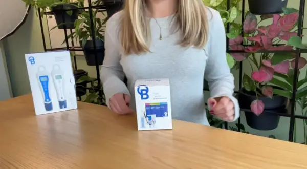 Kit di cura per sonde BlueLab con misuratori pH e conducibilità, su un tavolo di legno con piante sullo sfondo.