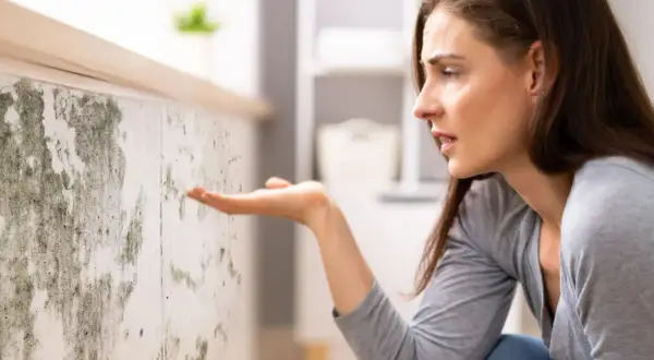 Donna preoccupata osserva muffa su muro, sintomo di umidità 70 per cento in casa.