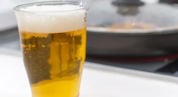 Un bicchiere di birra dorata con schiuma, accanto a una padella coperta. Forse la birra è un fertilizzante per le piante in cucina?
