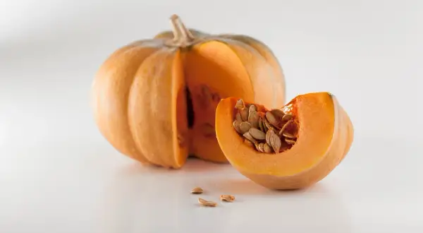 Zucca intera e una fetta con semi, pronti per imparare come piantare i semi di zucca e far crescere un orto autunnale.