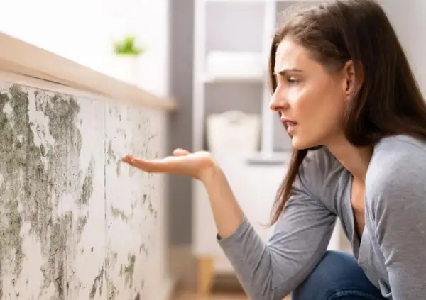 Donna preoccupata osserva muffa su muro, sintomo di umidità 70 per cento in casa.